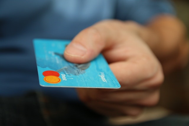 A hand holding out a credit card in order to donate money